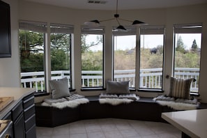 A corner seating area with a view of a deck and trees, a ceiling light fixture, and a kitchen counter.