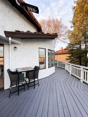 A deck with a table and chairs, a white textured wall, and a view of trees and a building in the background. - Luxury Home with Mount Shasta Views, Pool and Spa (Redding)