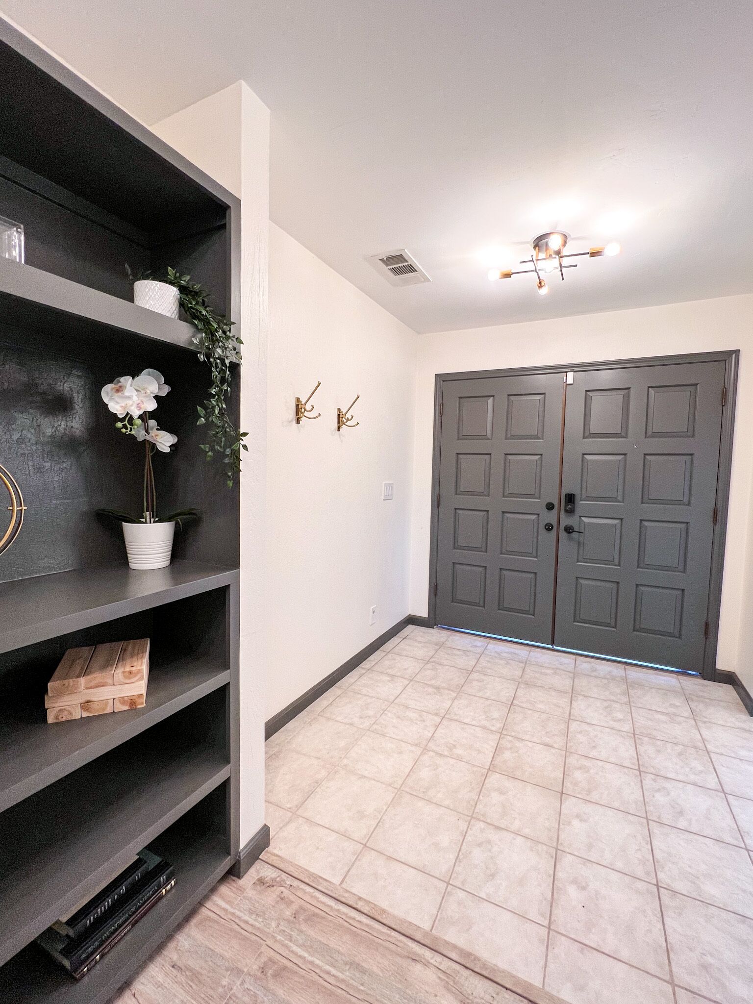 A hallway with a dark wood floor, a white wall, and a gray door.