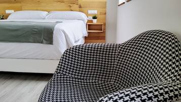 A bedroom with a wooden headboard, a bed with white bedding, a houndstooth patterned armchair, and a small bedside table with a plant.
