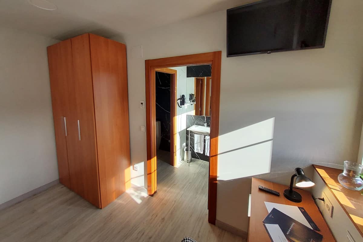 Ein Zimmer mit einem Holzkoffer, einem Schreibtisch mit Lampe, einem an der Wand befestigten Fernseher und einem Spiegel.