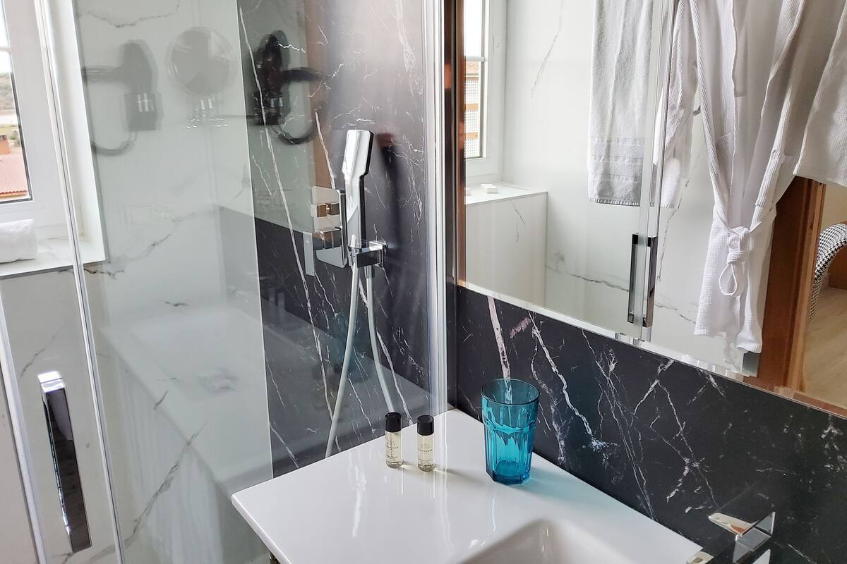 Ein modernes Badezimmer mit einer begehbaren Glasdusche, einem weißen Waschbecken und einer Marmor-Spritzschutzwand.