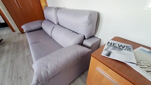 A grey sofa with a wooden side table beside it, featuring a magazine. - Hotel Marqués de Aguilar (Aguilar de Campoo)