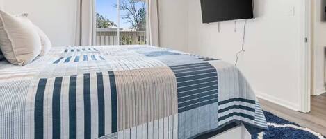 Un dormitorio con cama, televisión montada en la pared y ventana con cortinas.