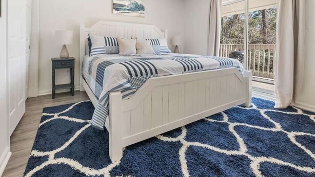 Un dormitorio con cama, mesita de noche, ventana con cortinas y vista al exterior.