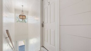 Una puerta blanca con el número 3, un candelabro y una ventana con vistas.