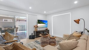 A modern living room with a large flat-screen TV, wicker side tables, and a sofa with cushions. - Ilanga Jervis Bay-Heated Pool (Huskisson)