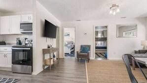 A modern kitchen with white cabinets, a built-in oven, and a flat-screen TV.