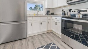 A modern kitchen with white cabinets, stainless steel appliances, and a window providing natural light.