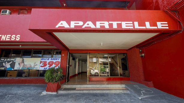 A red building with a sign reading "APARTELLE" and a large window displaying a sign for "OVER NIGHT 399". - Busline Apartelle (Quezon City)