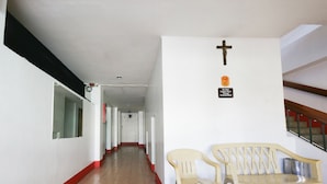 A corridor with a cross on the wall, a sign advising not to leave unattended items, and two plastic chairs. - Busline Apartelle (Quezon City)