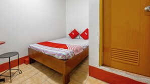 A small, single-bed room with a wooden bed, red pillows, a striped blanket, a small stool, and a wooden door. - Busline Apartelle (Quezon City)