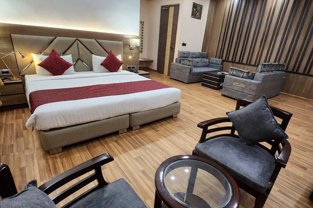 A modern hotel room with a large bed, a sofa, a coffee table, and a TV.