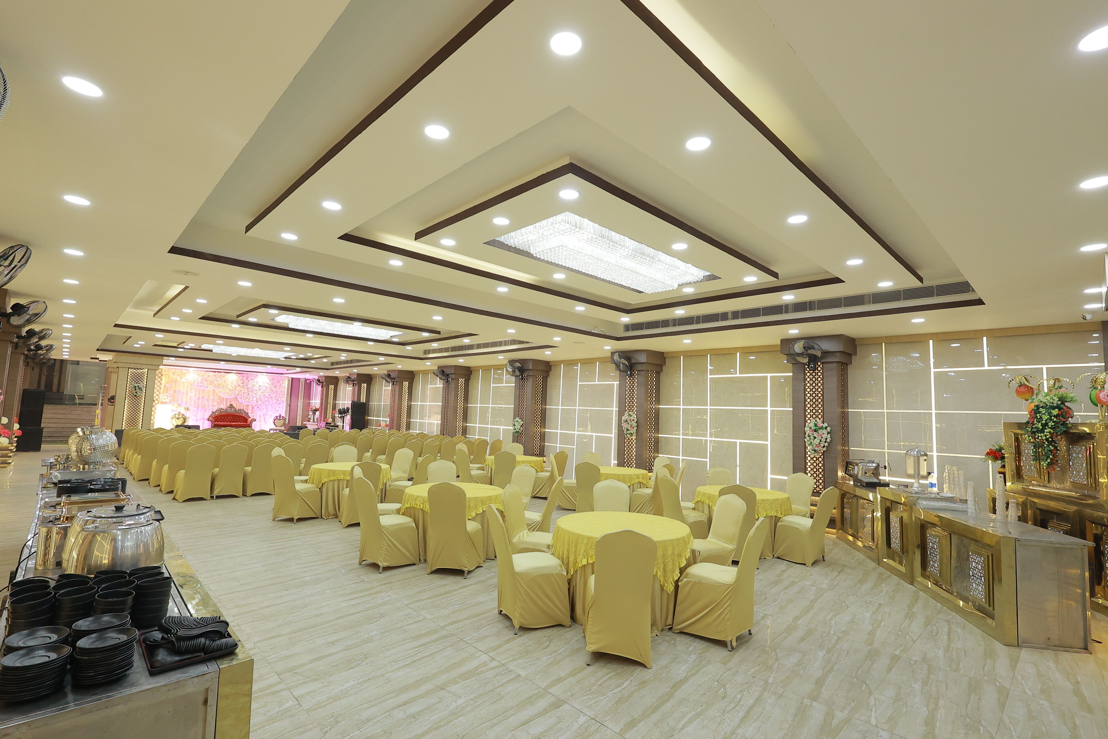 Een feestzaal met ronde tafels, bedekt met beige tafelkleden, in rijen gerangschikt.