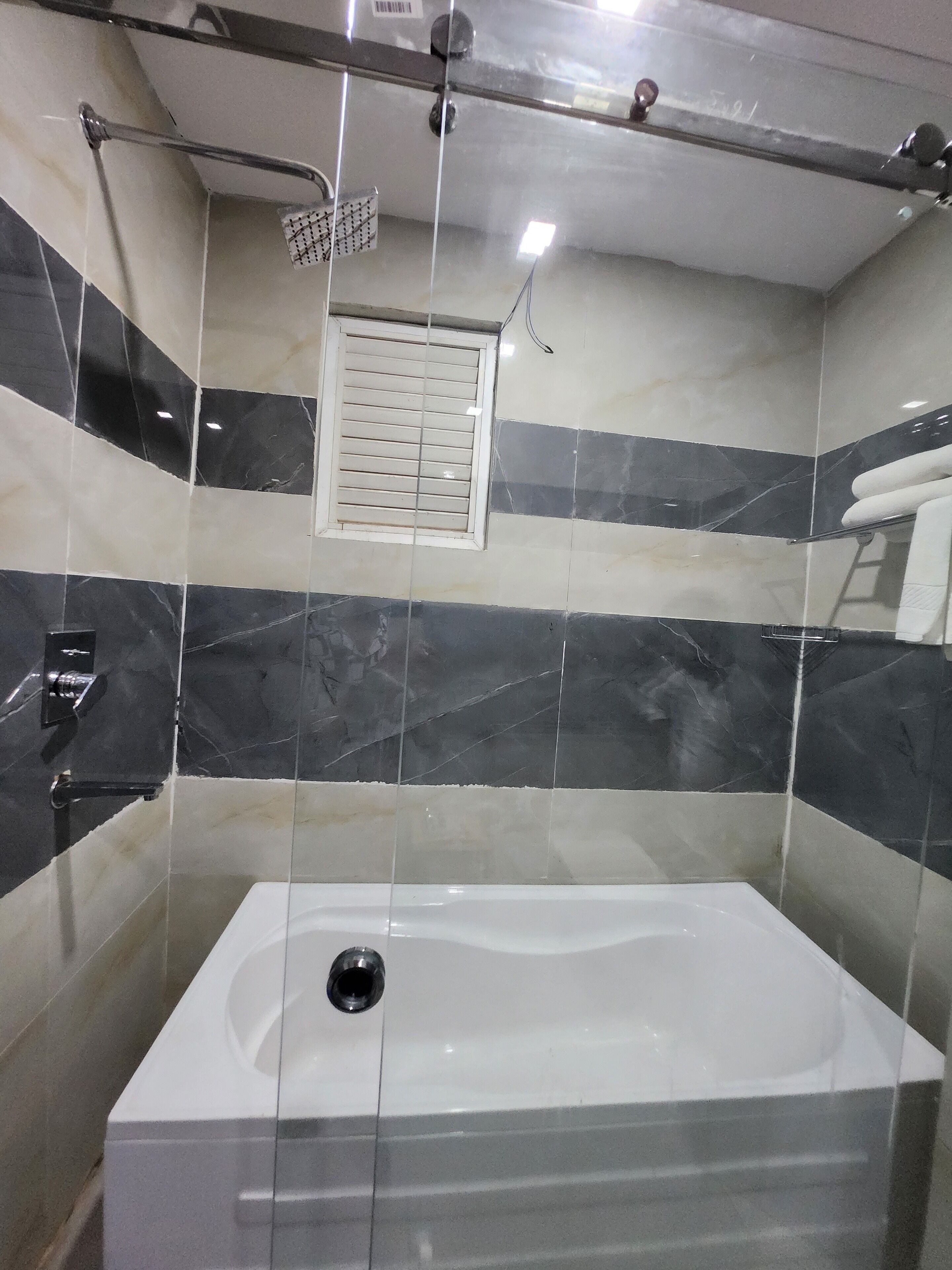Un baño moderno con una bañera rectangular, un cabezal de ducha y una ventana con persianas.