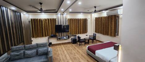 Habitación de hotel con sofá, cama, escritorio, televisor y aire acondicionado.