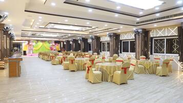 Un amplio salón de banquetes con filas de mesas y sillas redondas, un escenario con adornos florales y un diseño de techo moderno.