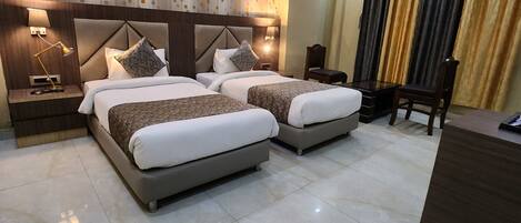 A hotel room with two beds, a desk, a chair, a ceiling fan, and a window with curtains.