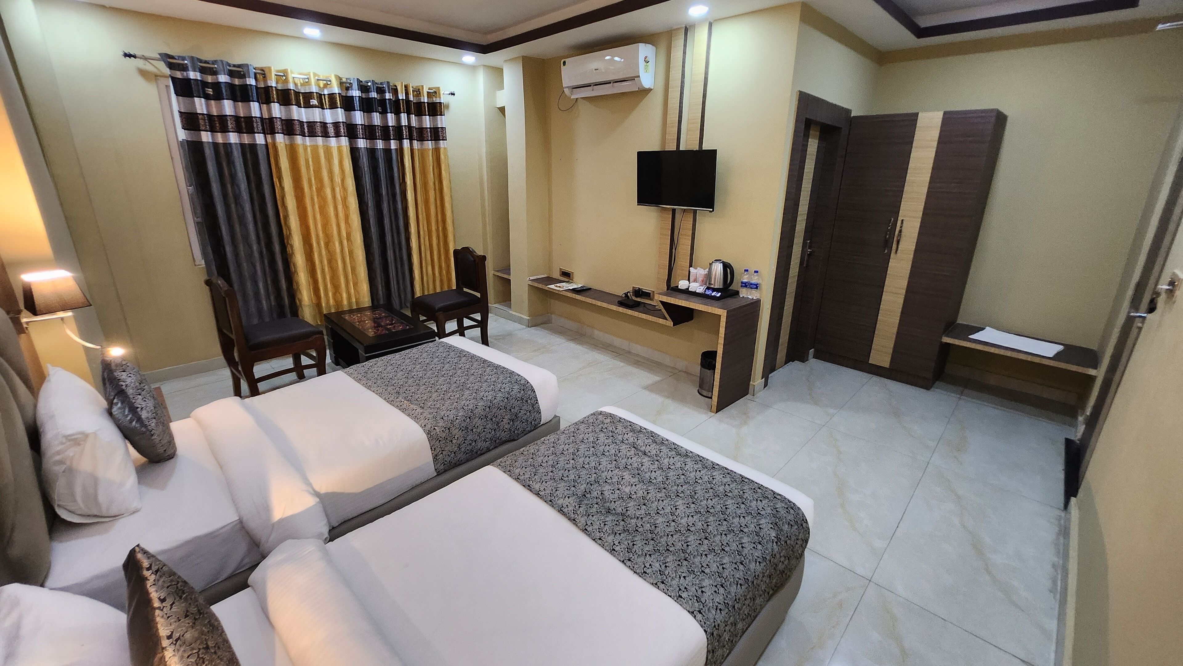 Une chambre d’hôtel avec deux lits, un bureau, une chaise, une télévision, un climatiseur et une armoire.