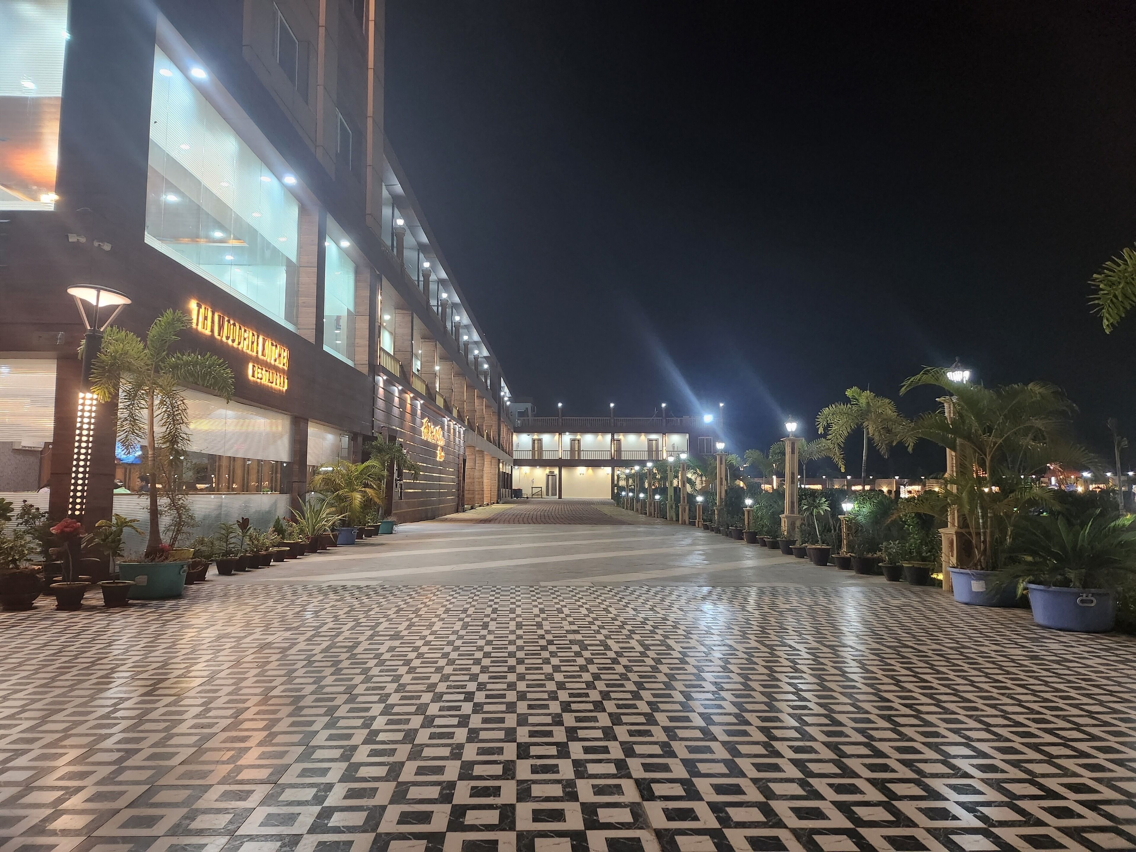 Un hotel con un camino empedrado, plantas en macetas y señalización iluminada.