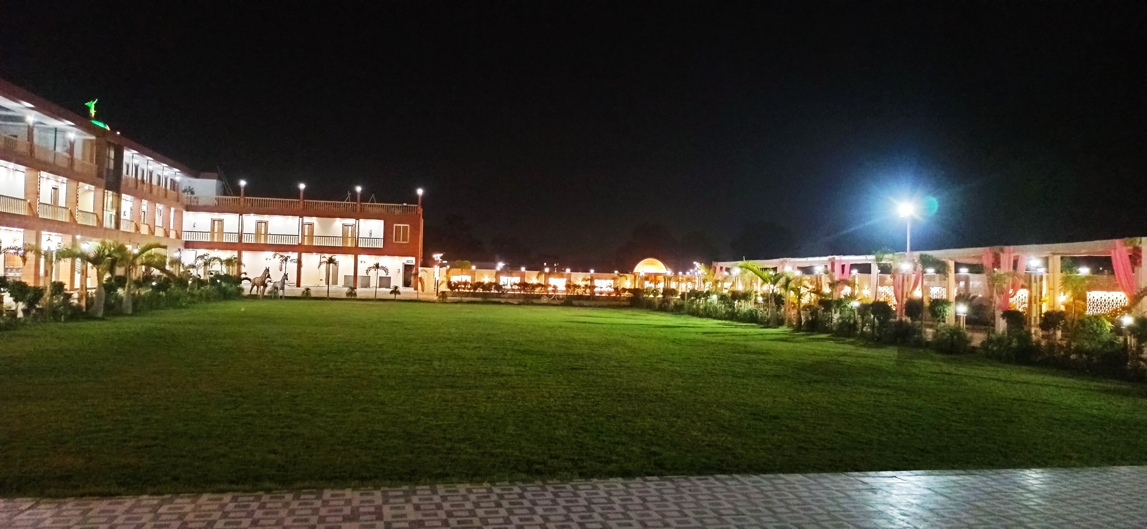 A hotel courtyard at night with a well-lit lawn and a large building with multiple balconies.