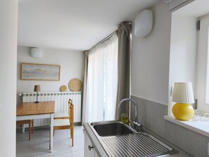 Une cuisine équipée d’un évier, d’une table en bois avec une chaise, d’un radiateur et d’une fenêtre avec des rideaux.