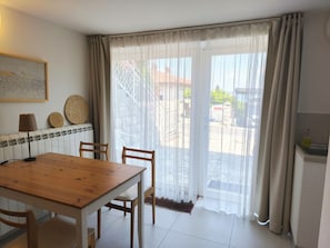Uma área de refeições com mesa e cadeiras de madeira, um radiador, uma luminária na parede e vista através de uma porta de vidro.