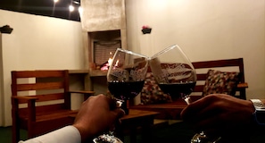 Two people toasting with wine glasses in a dimly lit room with wooden furniture and a fireplace.