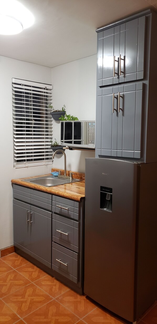 A kitchen with grey cabinets, a stainless steel sink, a built-in microwave, and a refrigerator.