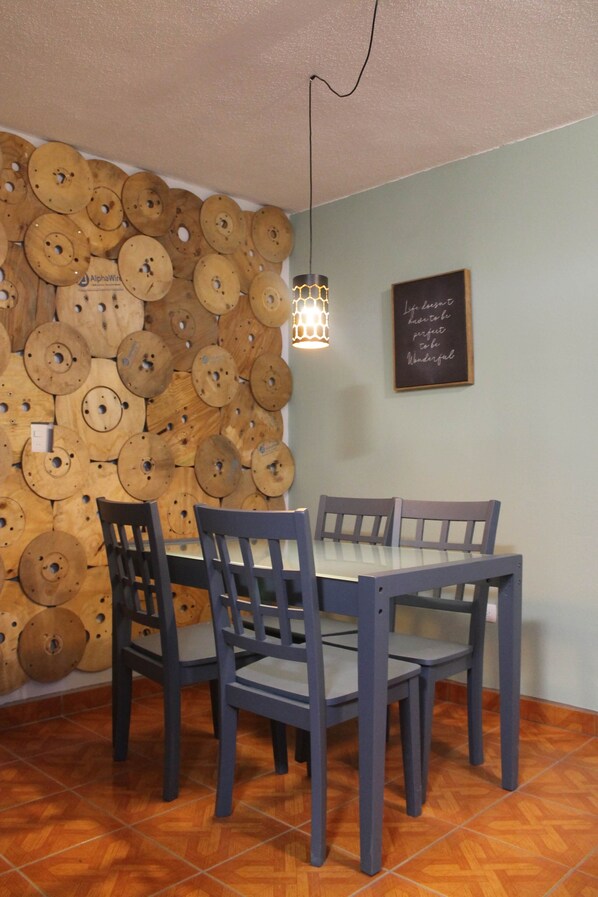A dining area with a wall of wooden plates, a table with four chairs, and a hanging light fixture.