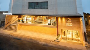 Un hotel moderno con fachada de color claro, múltiples ventanas y una entrada a nivel de calle con escaleras.