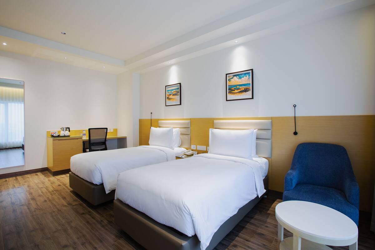 A hotel room with two beds, a desk, a chair, and a small table.