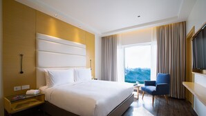 Habitación de hotel con una cama grande, televisión, una silla y ventana con vistas.
