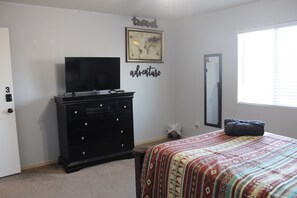 A bedroom with a bed, a dresser, a TV, a map, and a mirror.