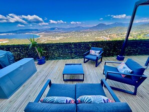 A deck with outdoor furniture, a grill, and a view of a coastal landscape.