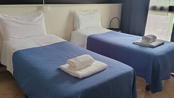 Two single beds with blue bedspreads, white pillows, and folded towels on the foot of each bed.