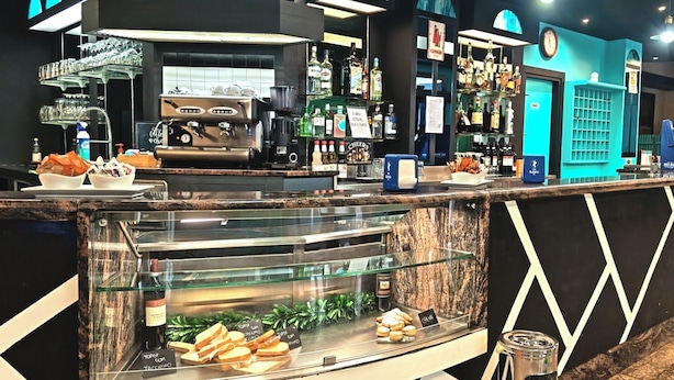 Un café proposant des expressos, une vitrine réfrigérée où sont exposées des pâtisseries, et une variété de bouteilles d’alcool.