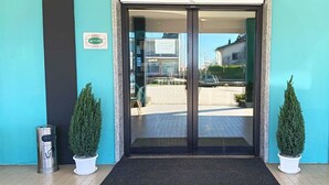 L’entrée d’un hôtel avec une porte en verre, des plantes en pot et une poubelle.