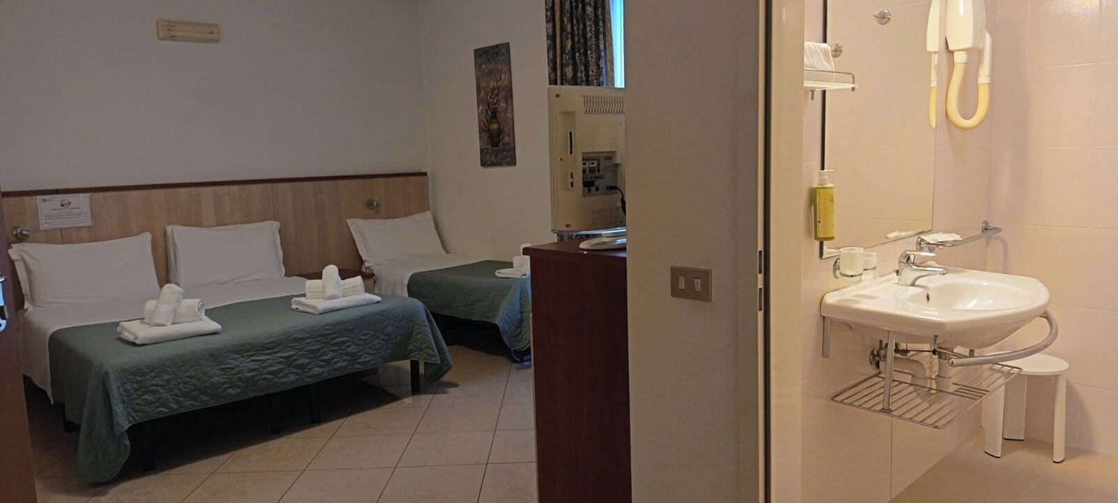 A hotel room with two beds, a small desk, a mirror, and a bathroom with a sink and toilet.