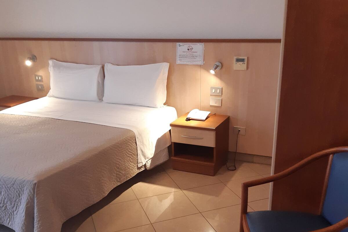Ein Hotelzimmer mit Bett, Nachttisch, Stuhl und Wandthermostat.