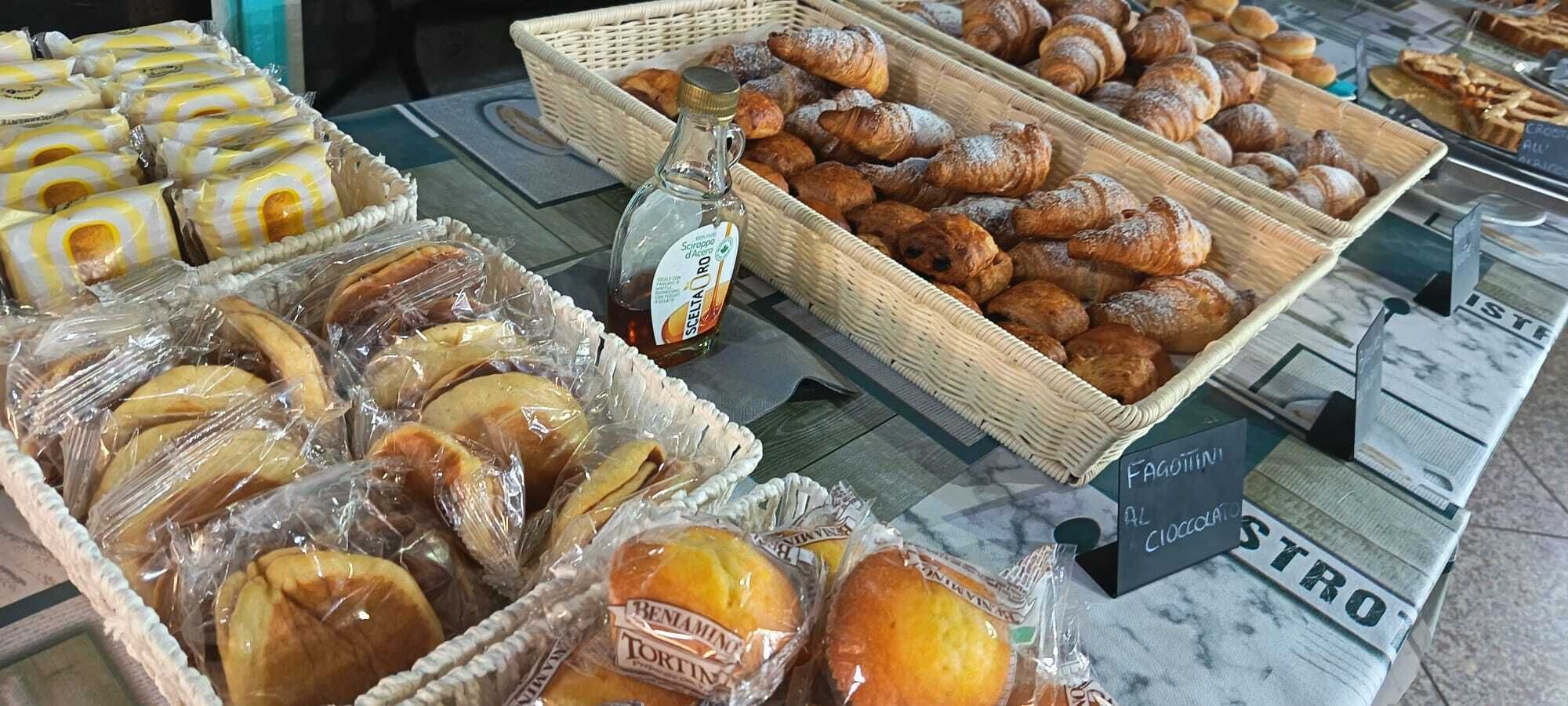 Una vitrina de panadería con diversos productos horneados, incluyendo croissants y pan, y un letrero que indica una opción de chocolate.