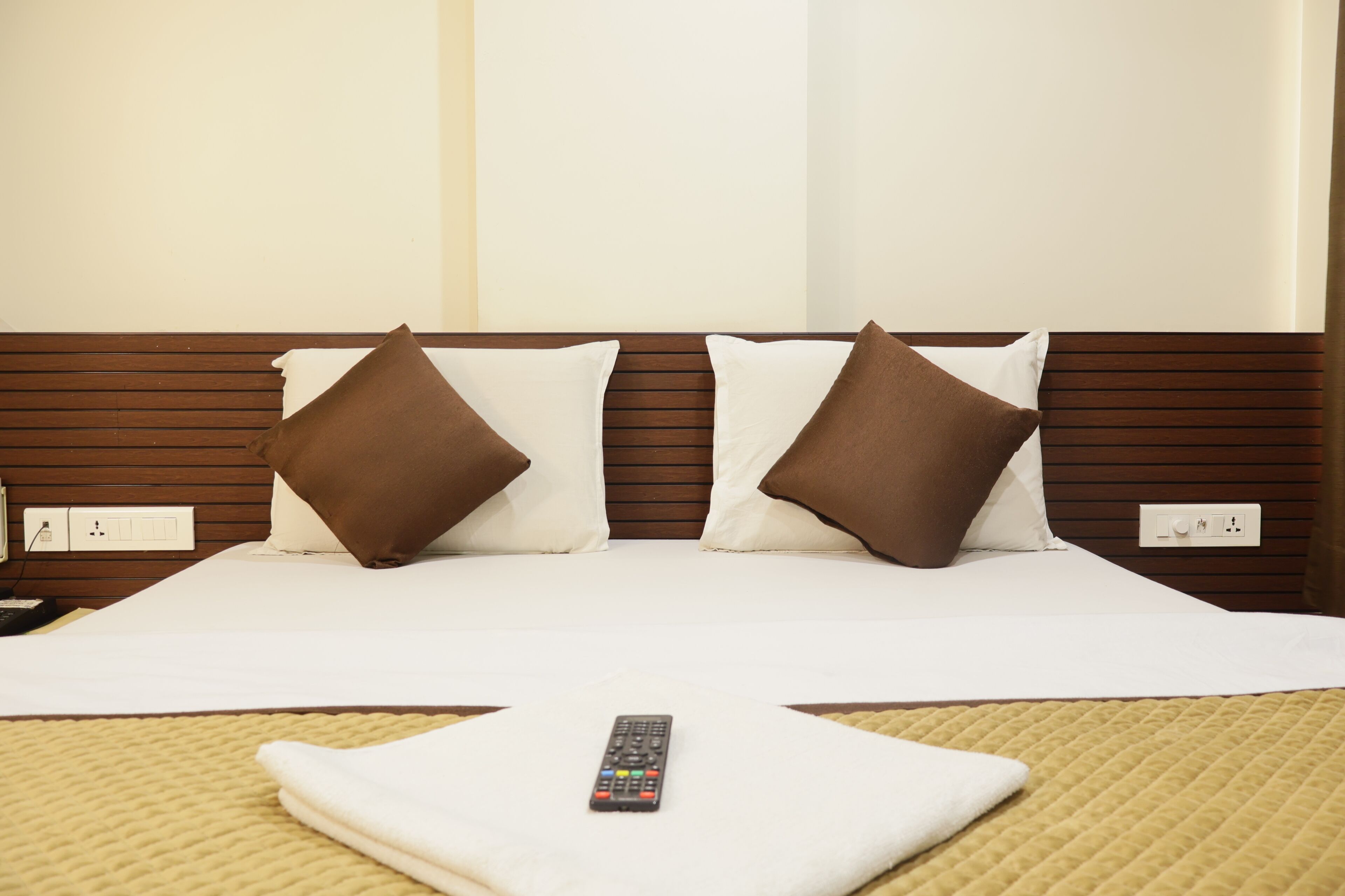 A neatly made bed with a remote control on the bedspread, two pillows, and a wooden headboard.