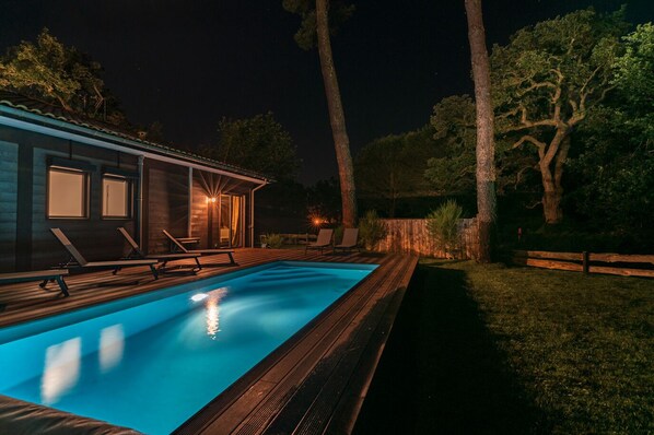 Une piscine dotée de chaises longues et d’une terrasse en bois, entourée d’arbres et d  ’une clôture en bois.