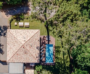 Vue aérienne d’une maison dotée d’un grand toit en pente, d’une piscine et d’un patio aménagé avec des sièges.