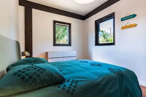 Une chambre à coucher avec un lit, deux fenêtres, une lampe de chevet et un panneau décoratif au mur.