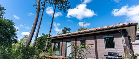 Ein modernes Haus mit Terrasse, Grill und hohen Bäumen im Hintergrund.