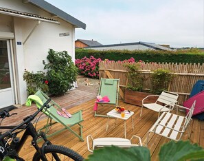 Una terraza de madera con asientos exteriores, una bicicleta y un perro.