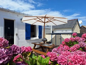 Un'area patio con un tavolo in legno, un ombrellone bianco e ortensie rosa.