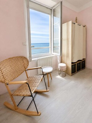 Une pièce avec un fauteuil à bascule, une petite table, une armoire et une vue sur la mer par la fenêtre.