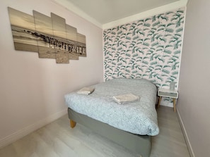 A bedroom with a bed, a wall-mounted artwork, a patterned wallpaper, and a small bedside table.